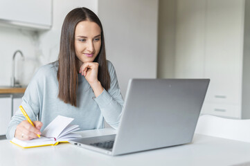 E-learning concept. Concentrated female student takes notes, writes down in notepad watching online...