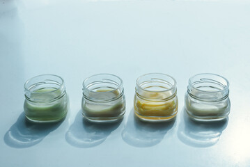 Row of four jars with cream on white surface in a hard light. Pastel colors and minimalism.