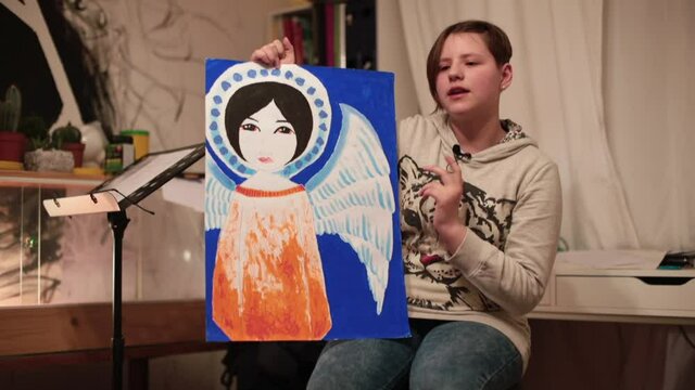 A teenage girl shows a drawn angel. She tells the story of the drawing. Oral history for the picture. Creative expression.