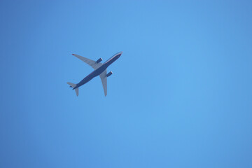 Fototapeta na wymiar Airplane flying on clear blue sky background. Passenger plane is gaining altitude