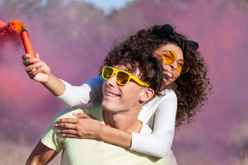 Beautiful young man and woman hold light up colored smoke bombs - Happy friends having fun in the...