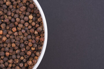 White glass bowl of black pepper. Isolated on a dark grey background. Top view close up