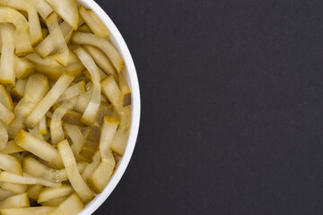 White glass bowl of sliced salted cucumber. Isolated on a dark grey background. Top view close up