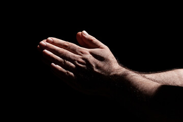 Fototapeta premium Male hands folded in prayer in the sunlight with harsh shadows, surrounded with darkness 