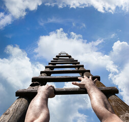 Muscular male hands gripping wooden ladder and reaching to the top, to the blue sky with white...