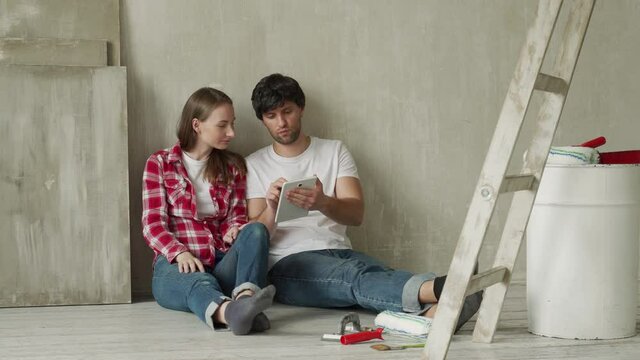 Family couple using digital tablet during renovation in new house. Young couple sits on the floor and using a tablet in a new home