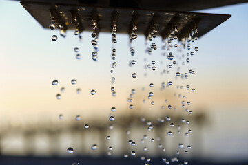 Water drops pouring from the outdoor beach shower head on blurred sunset seascape background, selective focus