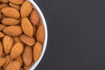 Almond in a white glass bowl. Top view photo of almond on dark grey background. Isolated close up photo