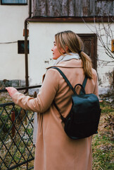 portrait of a beautiful Caucasian woman in the park, beige cashmere coat, black leather backpack, casual street style outfit, daily fashion