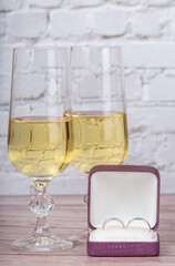 glass with champagne and wedding rings on bricks background