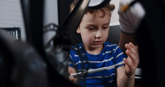 a cheerful baby boy in the house, repairing broken bicycle with tools