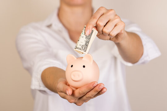 Woman putting dollar bancnote into piggy bank on light blue background, closeup. Space for text