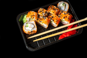 Traditional sushi and chopsticks. Philadelphia with salmon, avocado and cheese. Japanese cuisine on black background