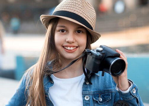 Girl wearing denim coat, straw hat and jeans with camera walking around city center and taking photos