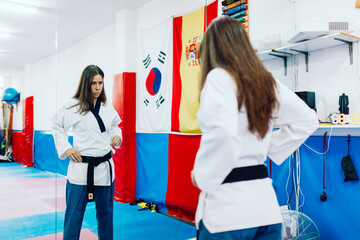 Young woman dresses in her taekwondo suit in front the mirror