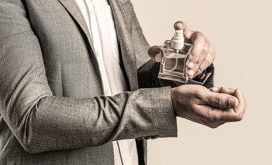 Men perfume in the hand on suit background. Man in formal suit, bottle of perfume, closeup. Fragrance smell. Men perfumes. Fashion cologne bottle