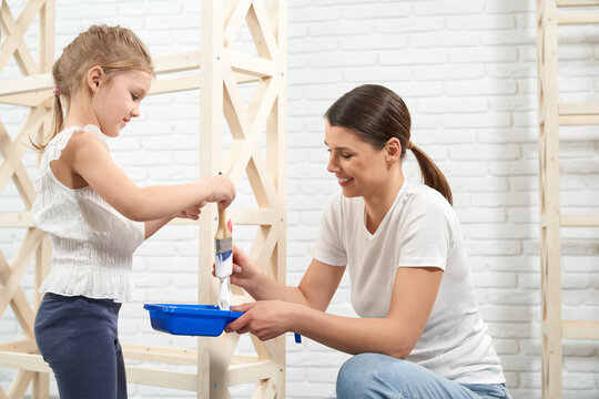 Close up of mother and daughter smiling and painting wooden rack. Concept of family time.