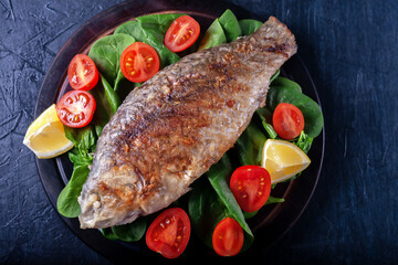 Grilled fish with tomatoes, spinach on a wooden board. Delicious and light dinner