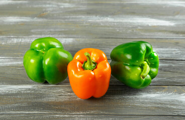 Three green and orange bell peppers on a wooden background.