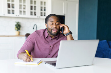 Multitasking and busy African-American male entrepreneur using laptop computer, talking on the...