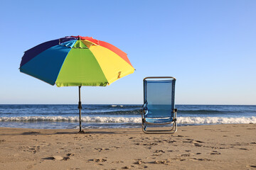 sombrilla de colores gay aislada puesta en la arena de la playa vacia con tumbona silla almería...