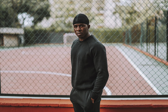 Black Spanish male in black casual clothes and do-rag posing in front of a wire fence