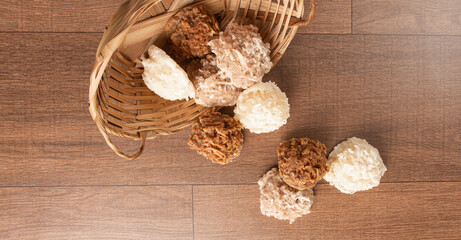 Cocada, Coconut candy from Brazil, white and brown cocadas fallen from a straw basket on wooden surface, black background, top view.