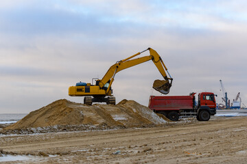 Fototapeta na wymiar Yellow excavator loads ground into the dumper. The road construction.