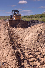 Obraz premium a bulldozer moves sand while building a dirt road to a new construction site
