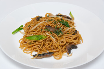Fried noodles,Chow mein,with the addition of mushrooms and vegetables on a white plate.