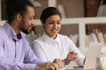 Close up smiling Indian businesswoman mentor training African American intern, pointing finger at...