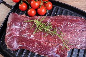 raw meat flecked with coarse salt and rosemary sprig on a cast iron plate