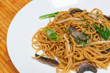 Fried noodles,Chow mein,with the addition of mushrooms and vegetables on a white plate.