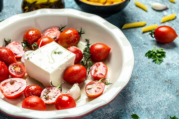 preparing tomato fetapasta. Oven baked cherry tomatoes and feta cheese with olive oil, garlic and thyme, cooking recipe ingredients, place for text, top view
