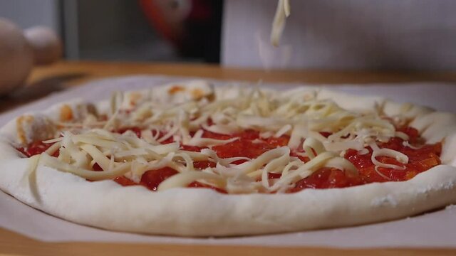 Hands are strewing grated cheese on pizza dought. Homemade cheese pizza with tomato sauce. Prepare tradition italian pizza at home. Close-up video. 