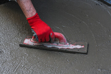 A man's hand in red gloves doing construction works on a cement ground home or outdoors on weekend...