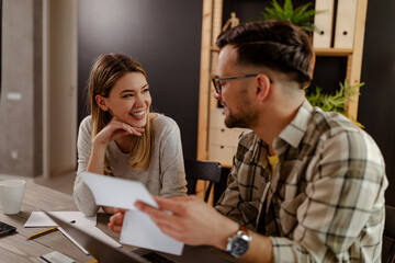 Young Caucasian smiling couple checking accountancy and bills while looking at each other.