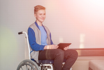 teen boy student sitting in a wheelchair while using a tablet at home.