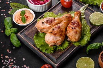 Tasty grilled chicken legs with spices and herbs on a wooden board on a dark concrete background