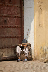 Man sitting in front of locked gateway with folded arms on the ground. You can't see his face. Does...