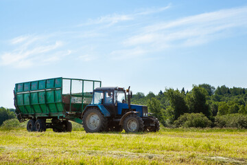 Tractor with a trailer in the field for agricultural work. Hay making, grassland. General plan, Copy space. 