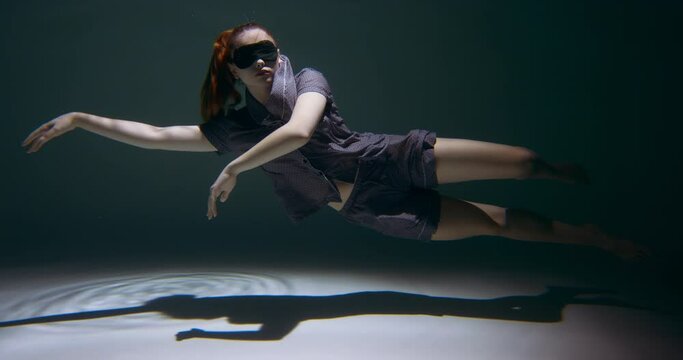 Healthy sleeping. Young beautiful woman wearing night pyjamas, sleep mask floats deep under dark water slow motion.