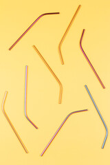Multicolored reusable stainless steel straws on pastel yellow background. Top view