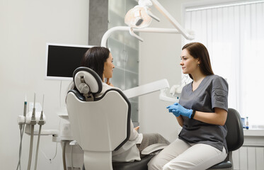 Friendly woman dentist consults a patient in an office in a modern dental clinic. The doctor listens attentively to the young woman