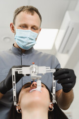 Fototapeta na wymiar An experienced dentist placing a facial bow for woman patient to examine the bite. Modern technologies in dental treatment