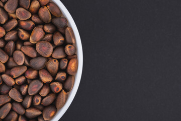 White glass bowl of pine nut. Isolated on a dark grey background. Top view close up
