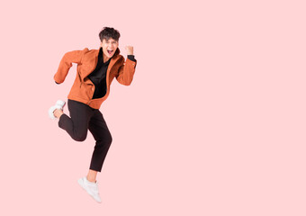 Happy handsome Asian man in fashionable clothing and jumping doing winner gesture isolated on pink...