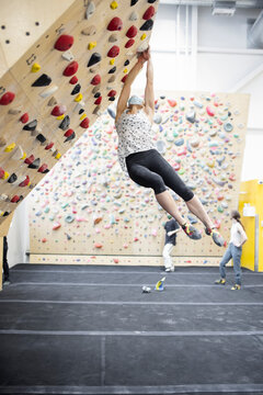 Female climber in face mask hanging from wall in climbing gym