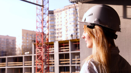 HardWorking beautiful woman builder in white helmet looking for construction site and crane
