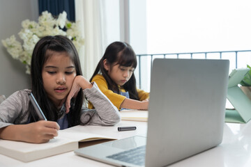 Little Asian girl studying online lesson at home with sister. Homeschooling during quarantine online education concept.